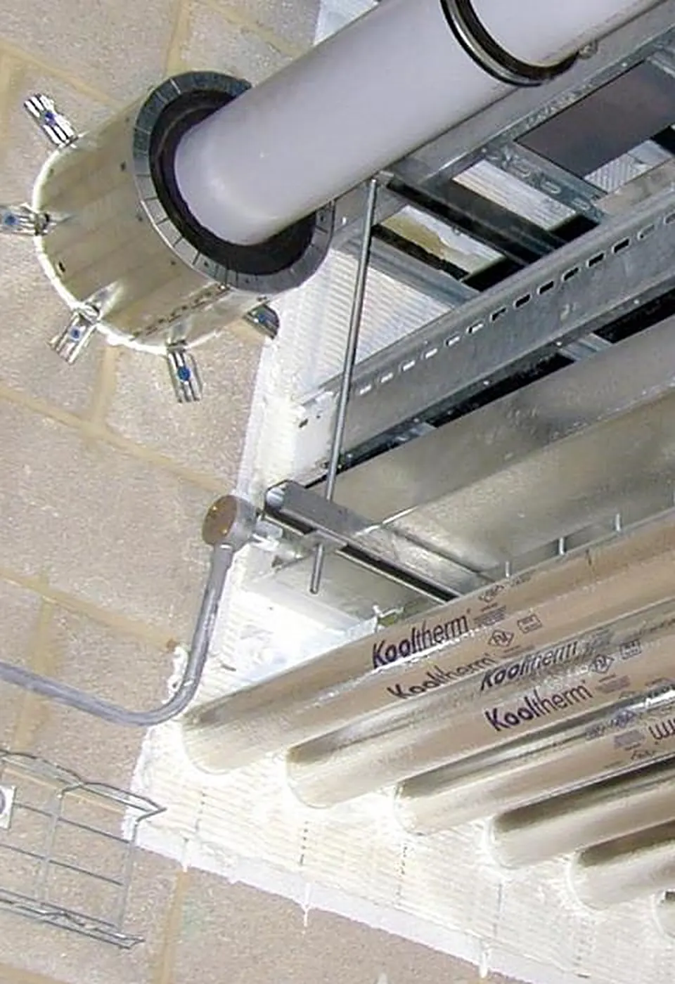 Close-up of fire stopping where insulated pipes pass through a fire-rated wall, sealed with fire batt and an intumescent pipe collar